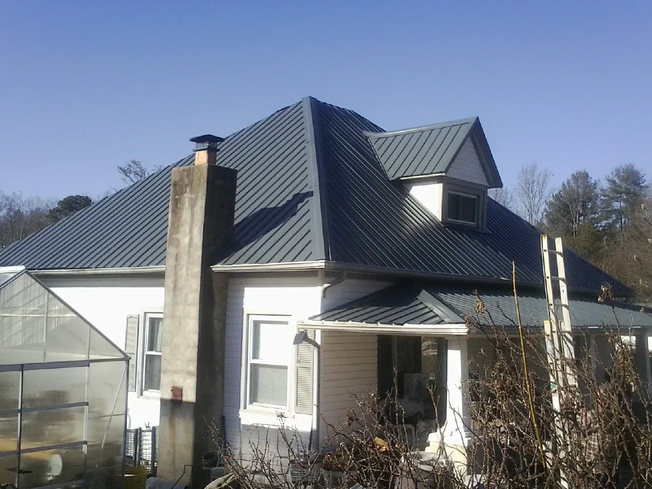 Dark blue standing seam metal roof on a white farmhouse with dormer — Slate & Tile Roof Repair by Roofing Brothers in Spring Park