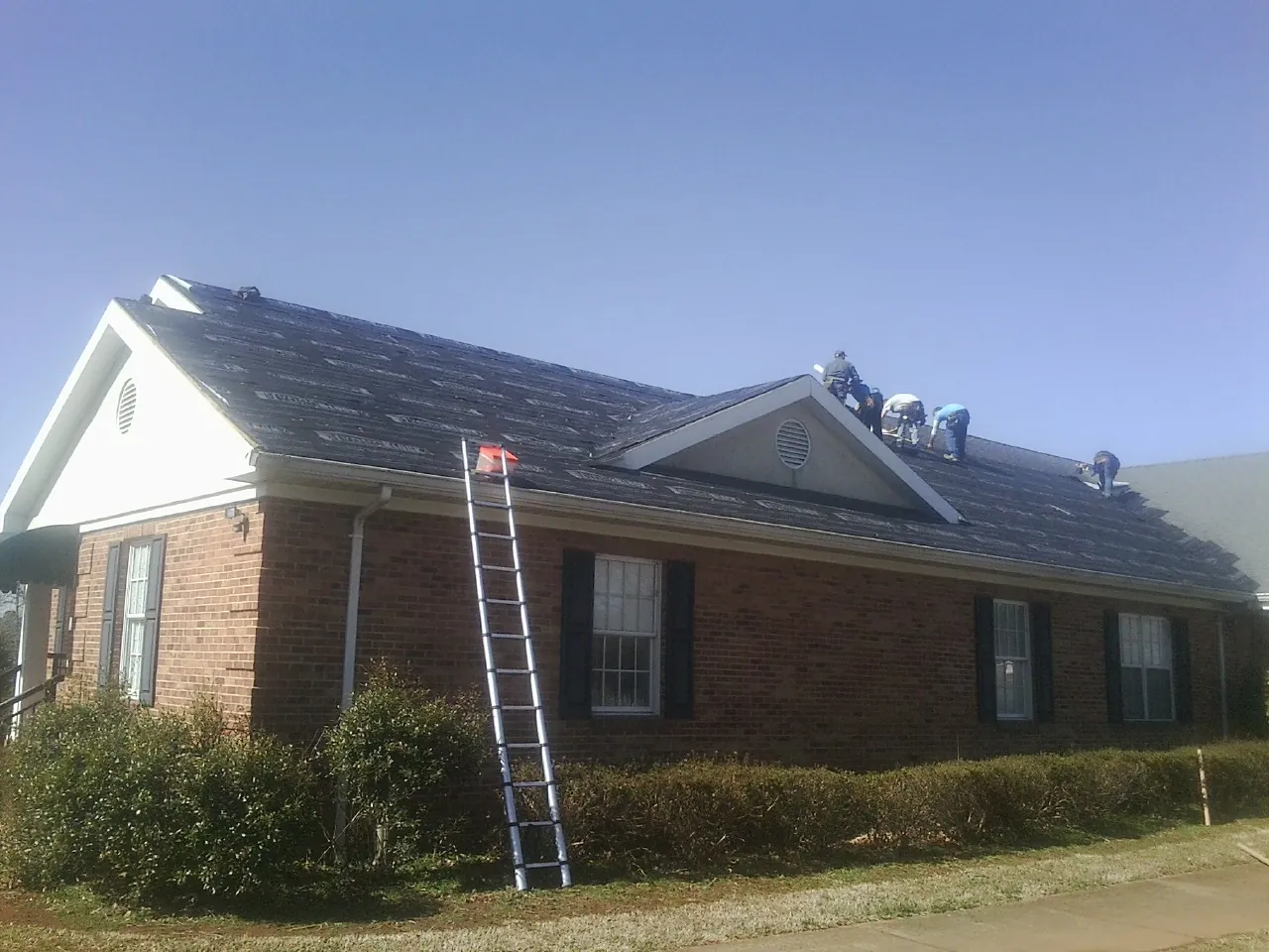 Crew tearing shingles off a brick ranch roof with a ladder set — Emergency Roof Repair work by our crew in Spring Park