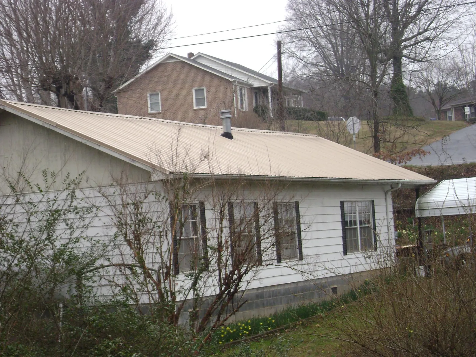 Tan metal roof on a white sided house set into a hillside — Commercial Roofing by Roofing Brothers in Spring Park